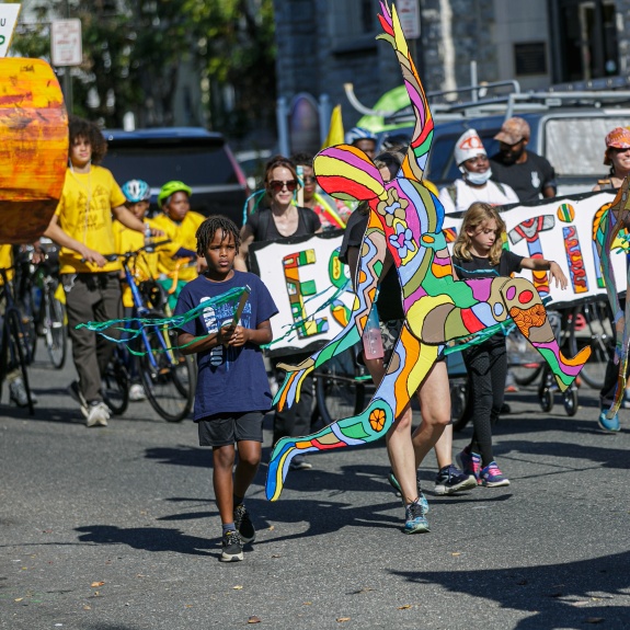Group of community members marching in Spiral Q's Peoplehood Parade in West Philadelphia with art work, puppets, and banners.